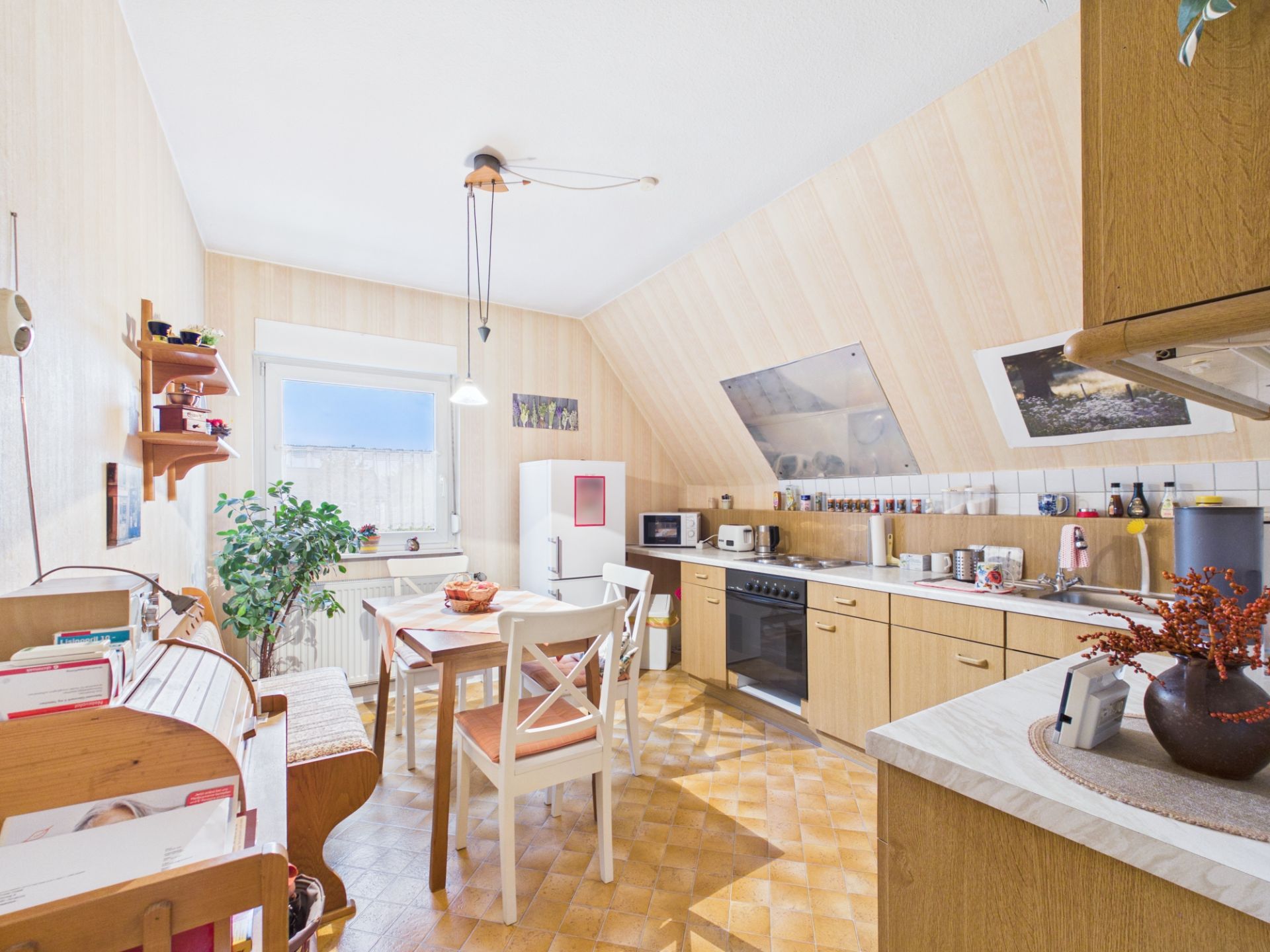 Helle Wohnküche mit Holzmöbeln, Esstisch, Pflanzen und Küchenzeile unter Dachschräge.