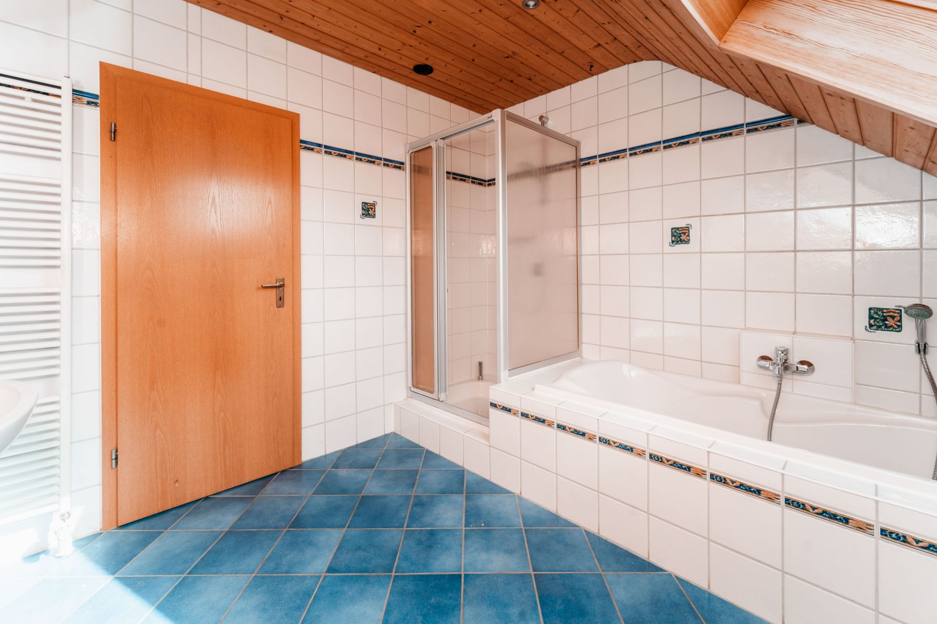 Badezimmer mit blauen Fliesen, Badewanne, Dusche und Holztür unter einer Holzdecke.