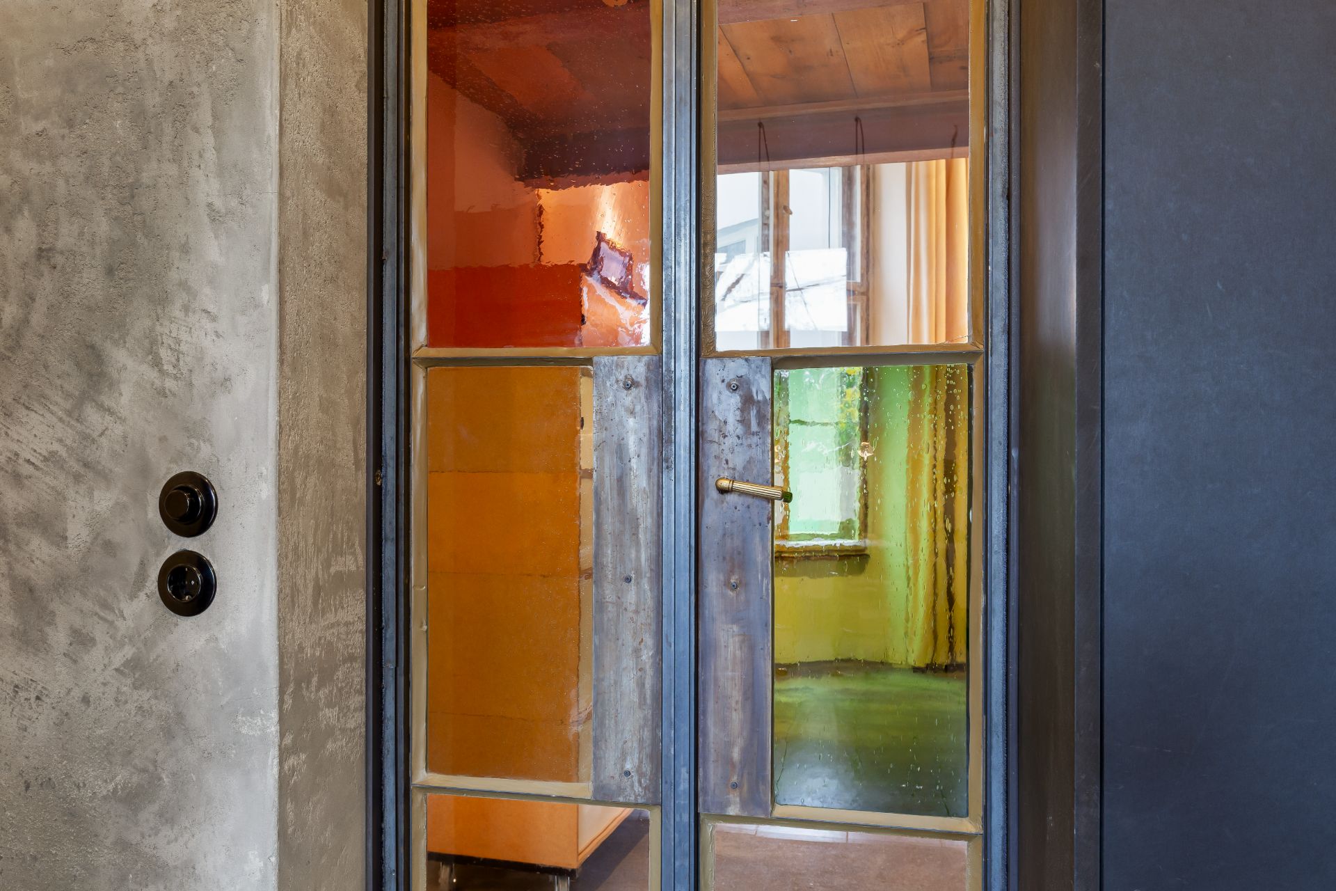 Holztür mit buntem Glas, dahinter farbige Räume und Fenster sichtbar.