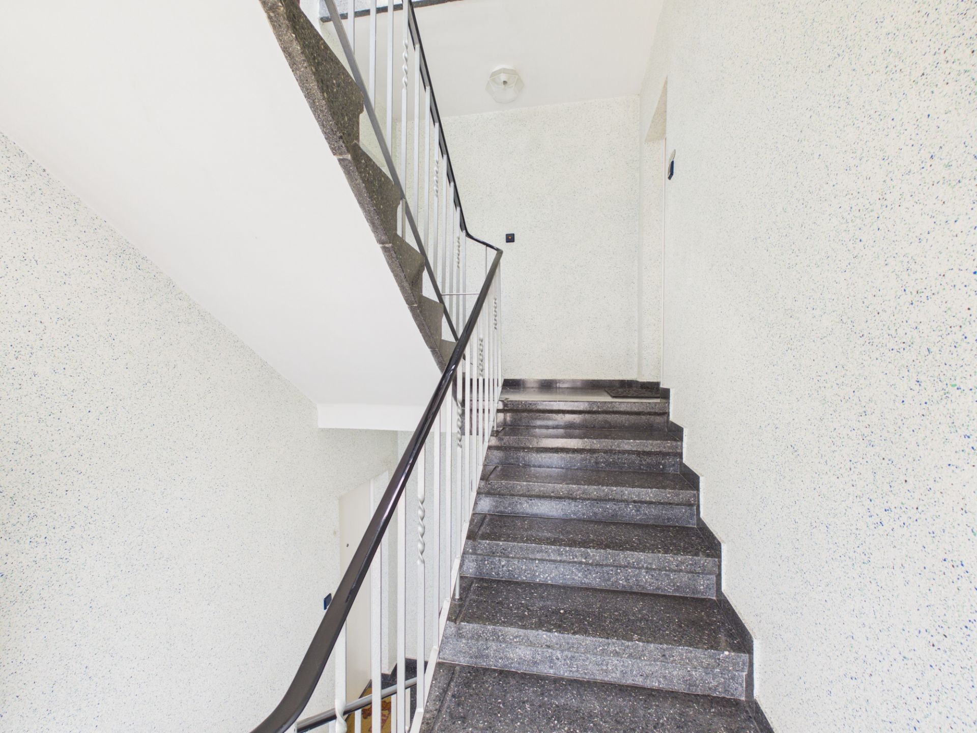 Graues Treppenhaus mit Metallgeländer in einem Wohngebäude.