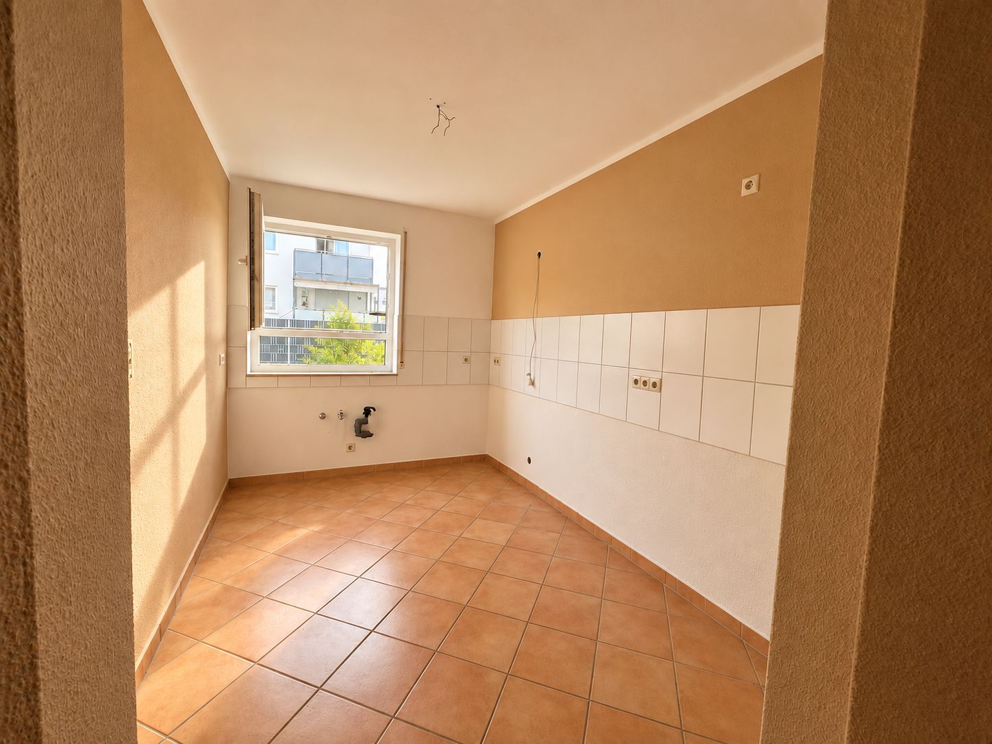 Leerer Raum mit Fliesenboden und gefliester Wand, Fenster mit Blick nach draußen.