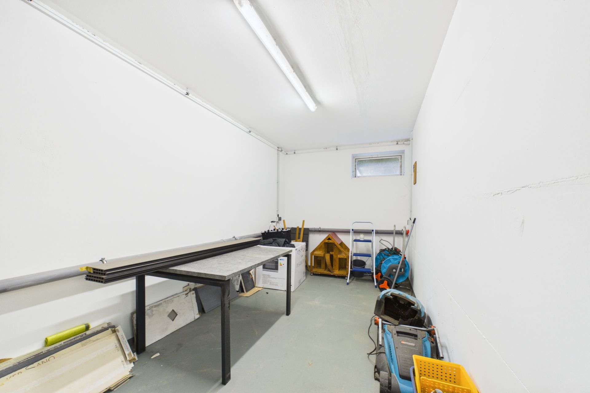 Heller Raum mit Werkbank, Werkzeugen, Leiter und kleinem Fenster an der Wand.