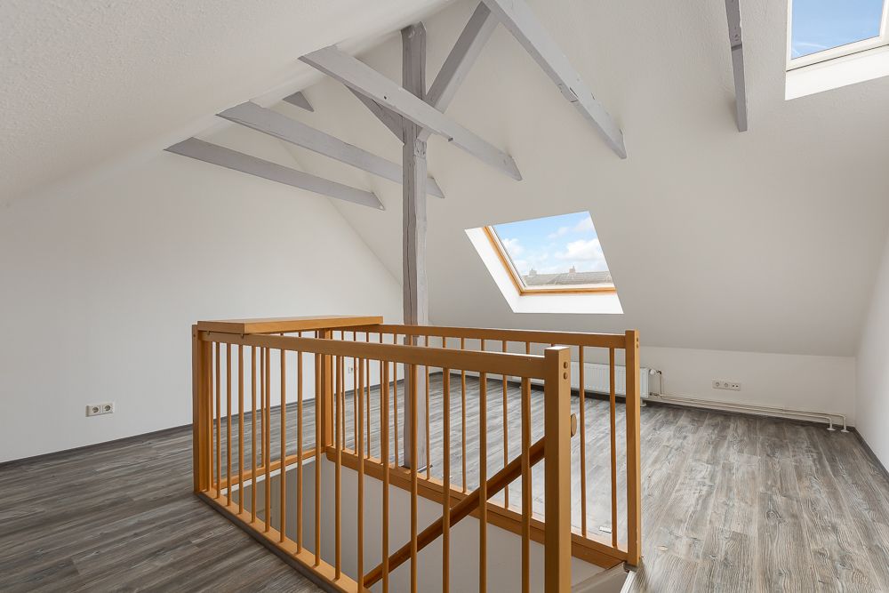 Heller Dachbodenraum mit Holzgeländer, Dachfenster und sichtbaren Balken.