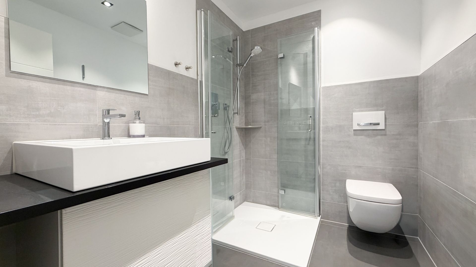 Modernes Bad mit Dusche, Waschbecken, Spiegel und WC, grau-weiße Fliesen.