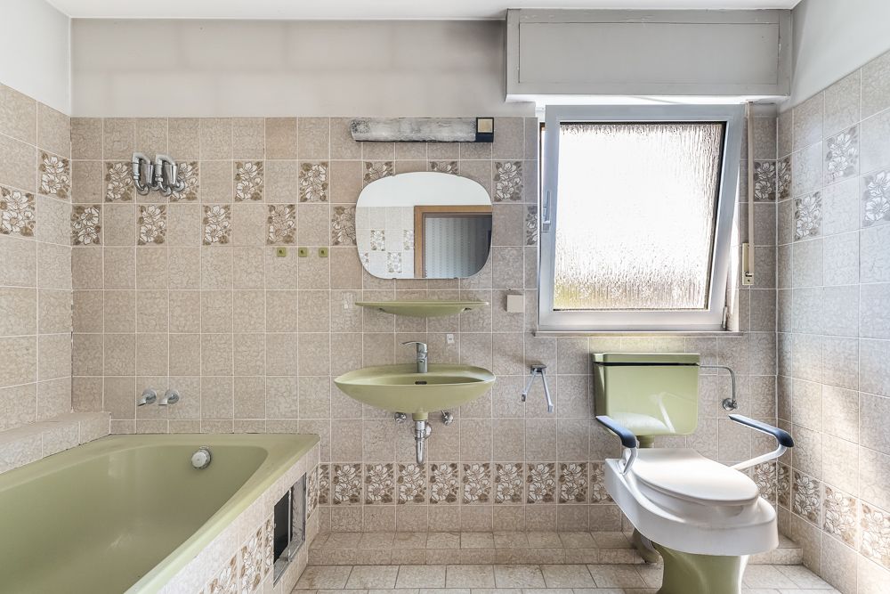 Badezimmer mit grüner Badewanne, grünem Waschbecken, Toilette und Fenster, beige Fliesen mit Blumenmuster.