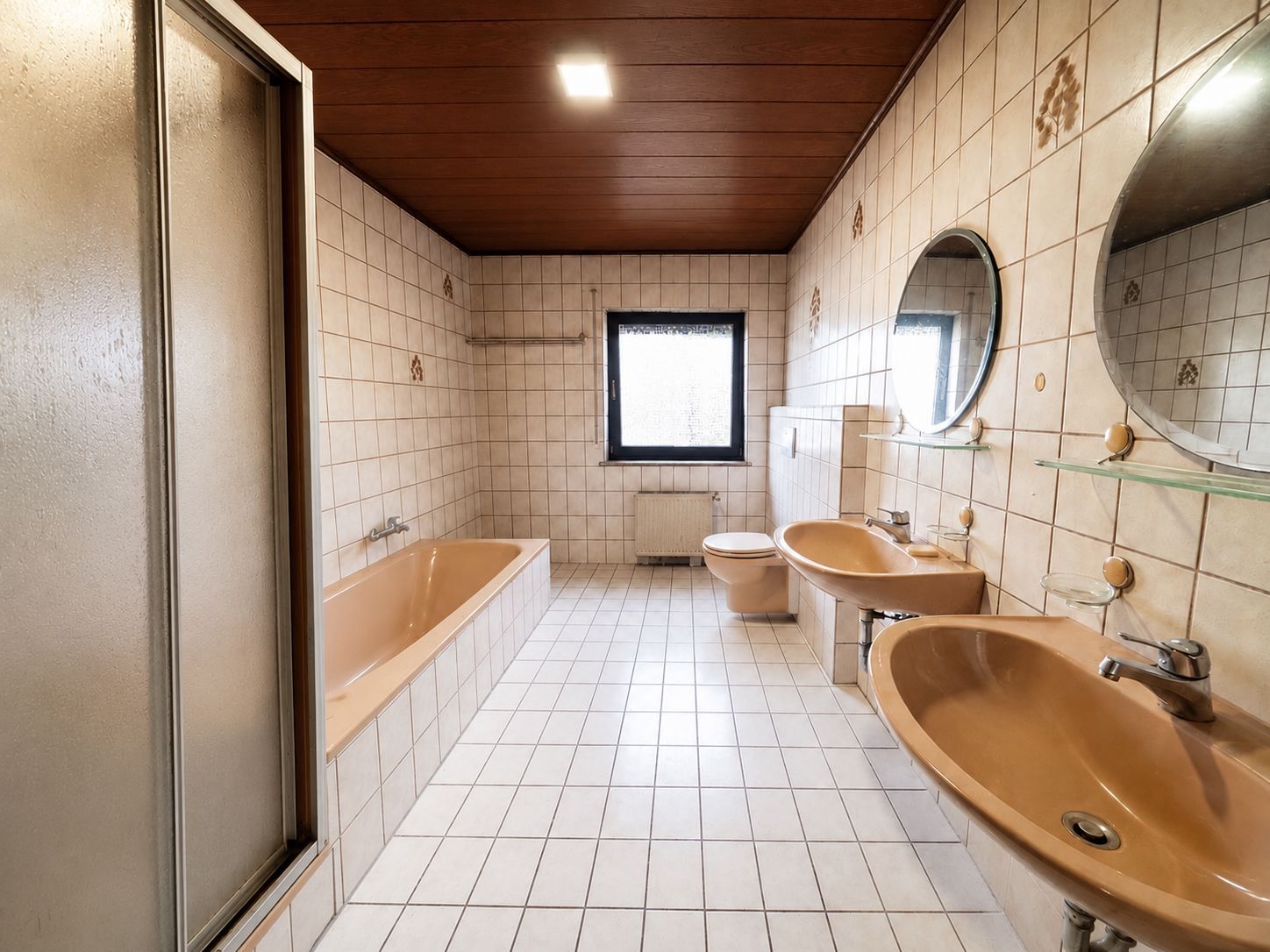 Badezimmer mit brauner Badewanne, zwei Waschbecken, Dusche, Toilette und Fenster.