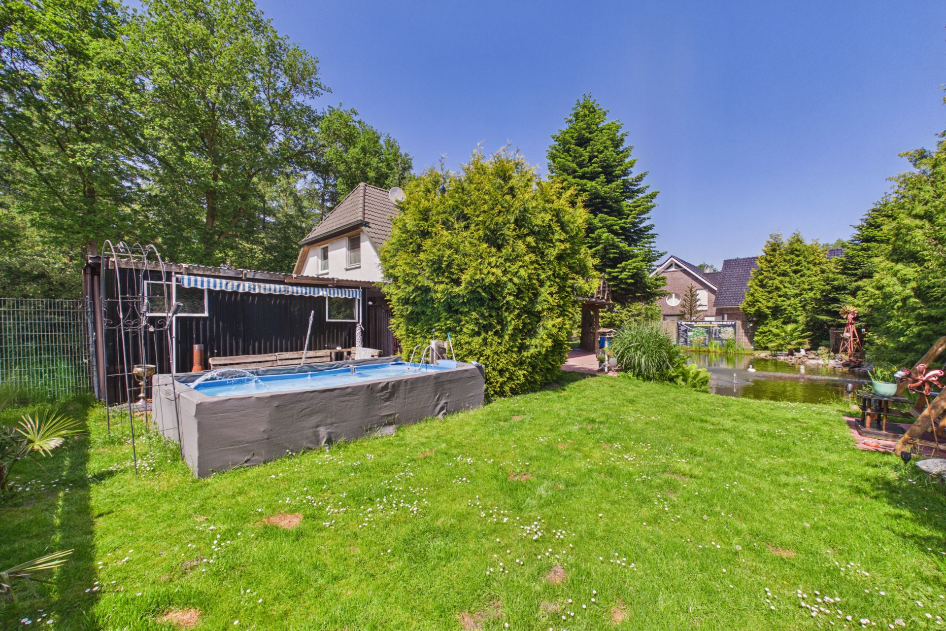 Garten mit Aufstellpool, Rasen, Bäumen und einem kleinen Teich vor einem Wohnhaus.