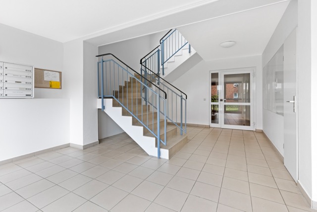 Heller Hausflur mit Treppenhaus, Briefkästen und Fliesenboden.