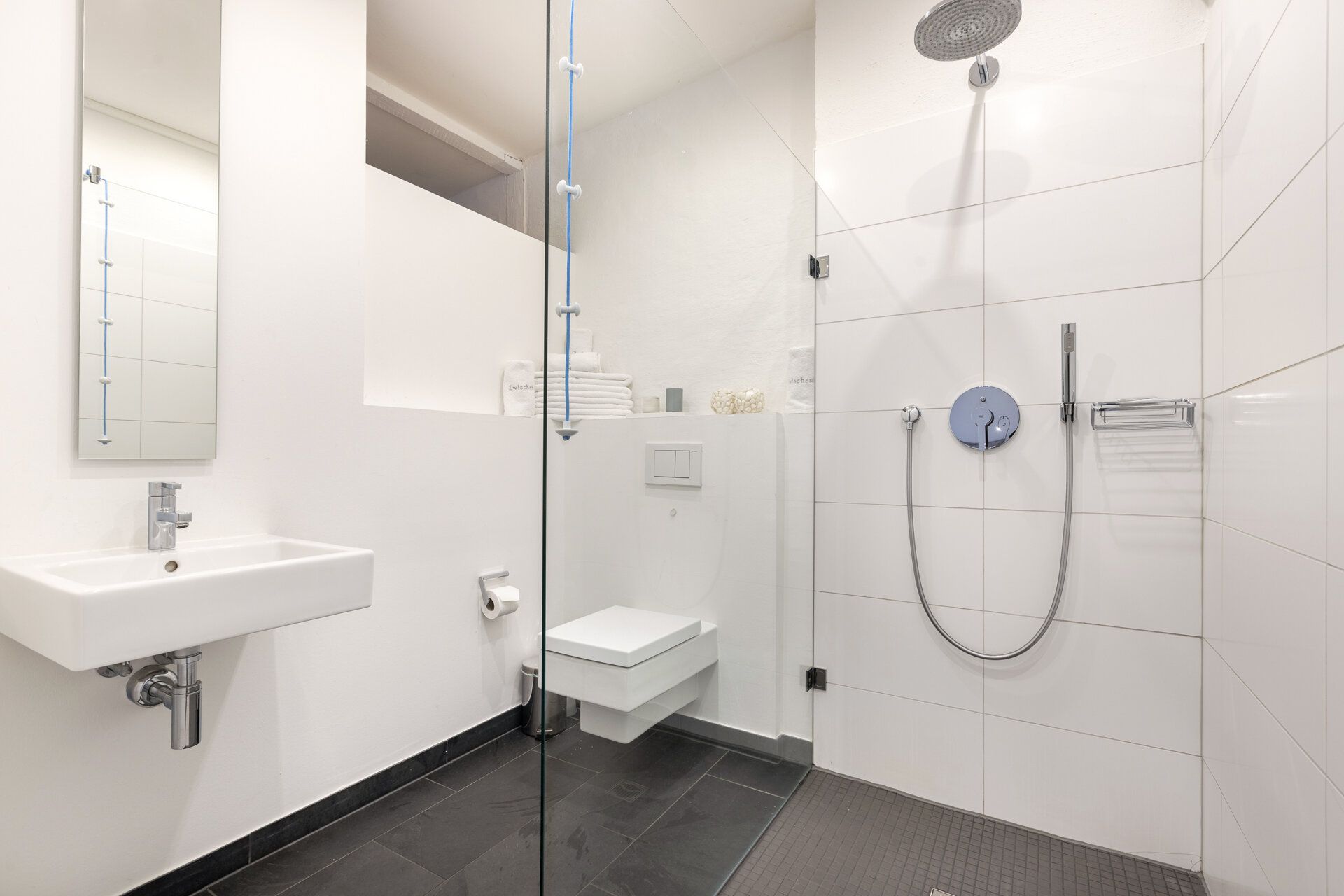 Modernes Badezimmer mit Dusche, Wandwaschbecken, Spiegel und wandhängender Toilette.