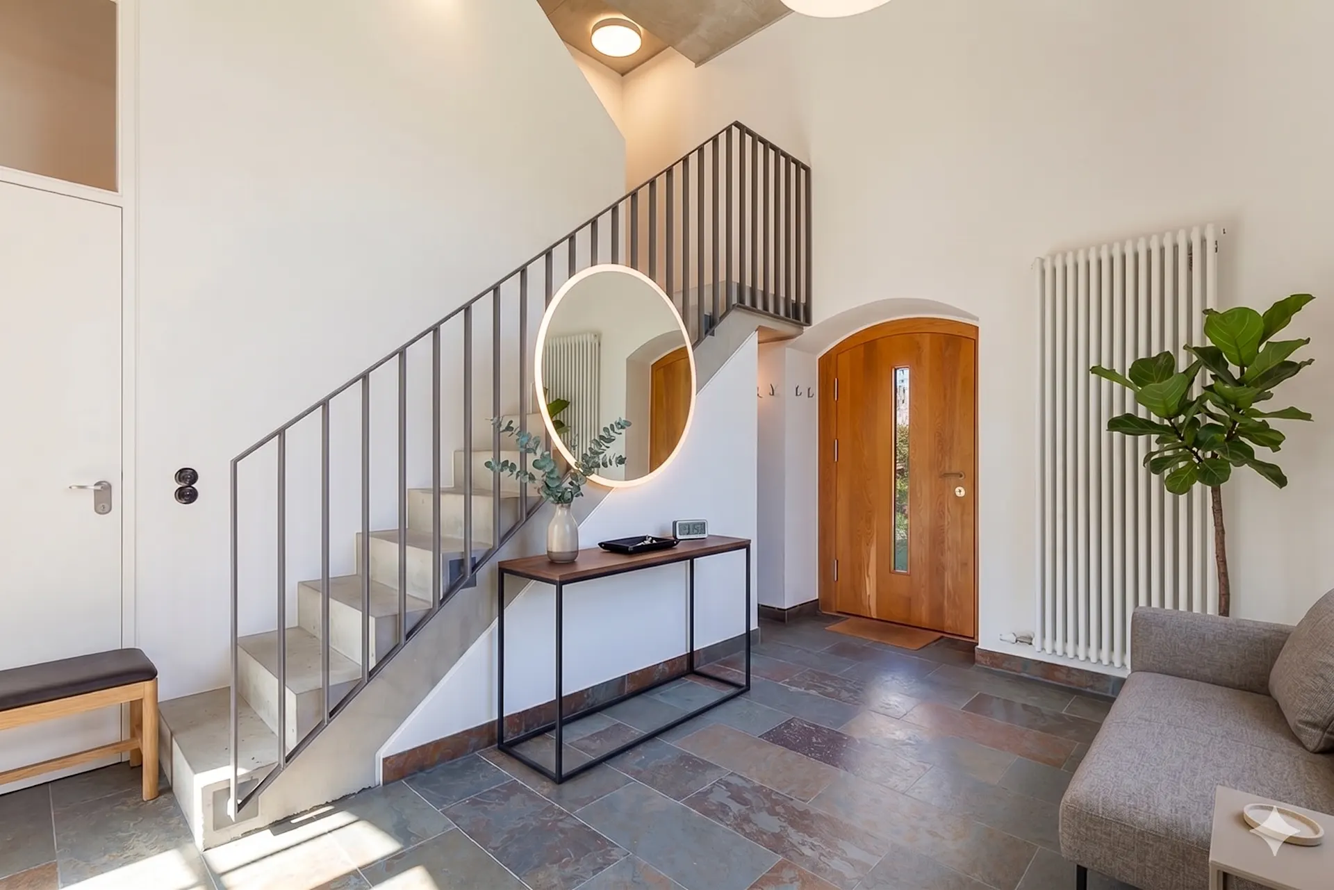 Heller Flur mit Treppe, rundem Spiegel, Holztür, Sofa und Zimmerpflanze.