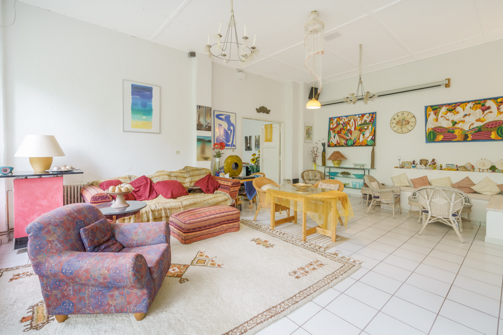Helles Wohnzimmer mit Sofa, Sesseln, Esstisch, Teppich und farbenfroher Wandkunst.