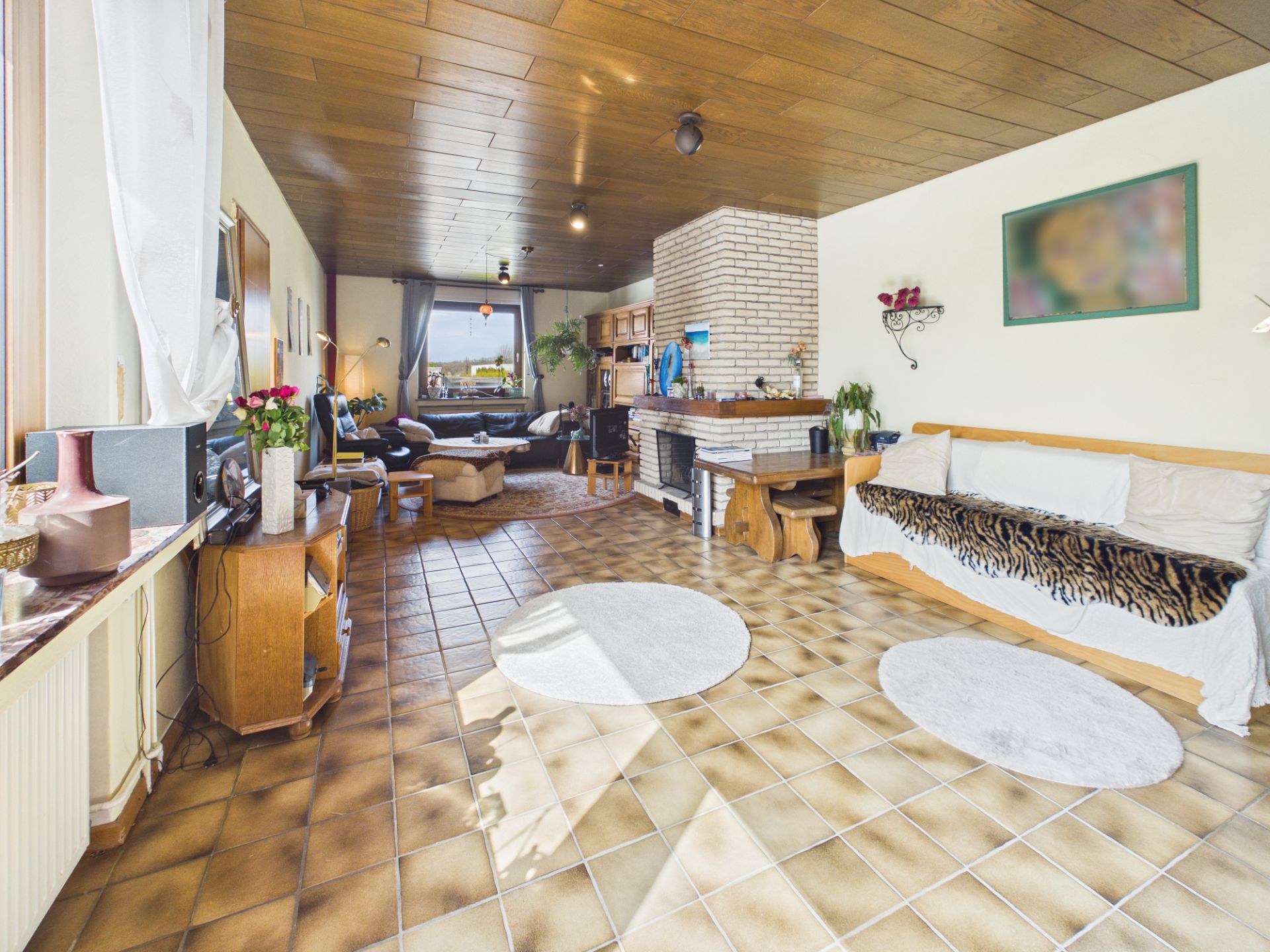 Helles Wohnzimmer mit gemustertem Fliesenboden, Kamin, Sofaecke und großen Fenstern.