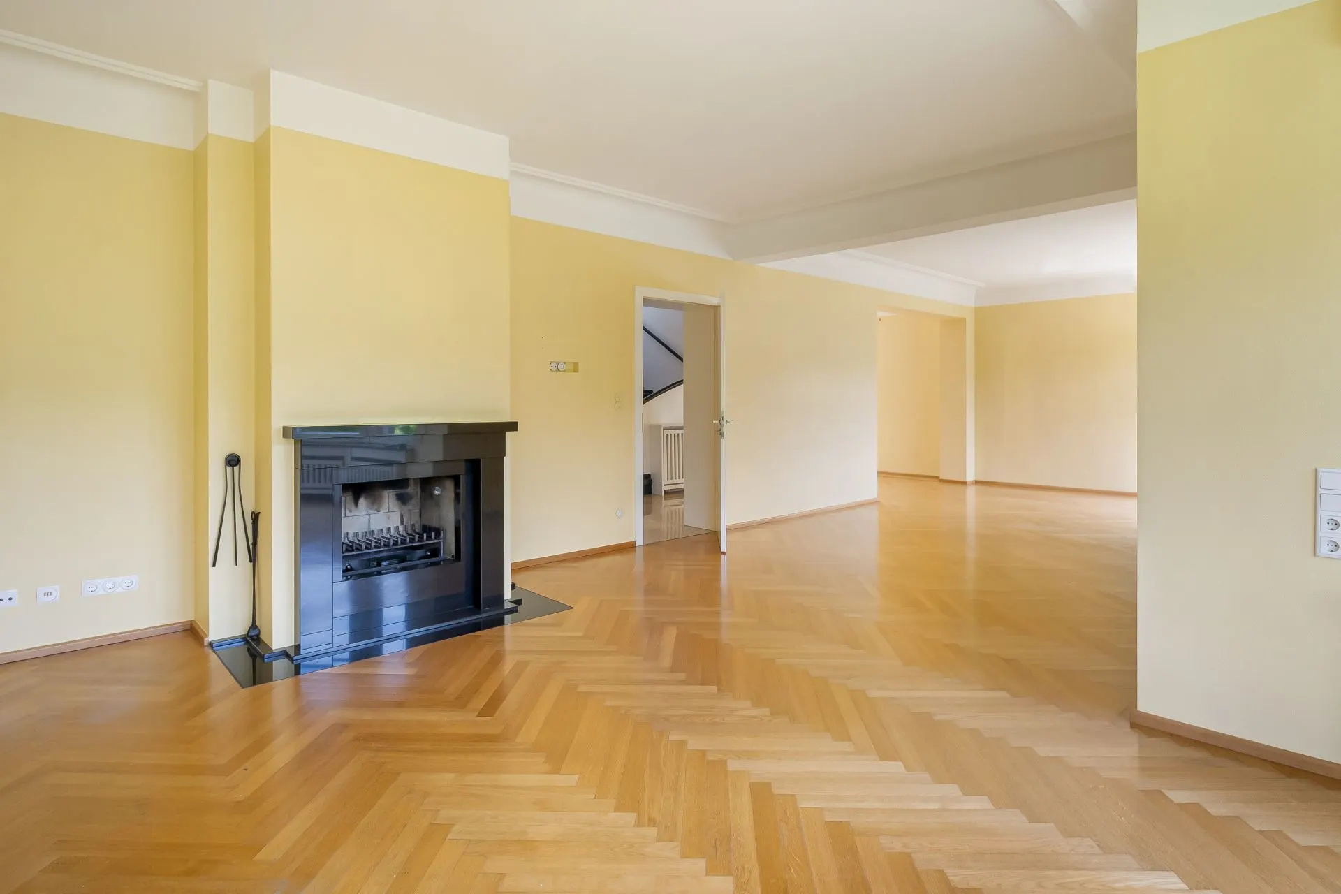 Helles Wohnzimmer mit Parkettboden und Kamin, offene Tür führt in einen weiteren Raum.