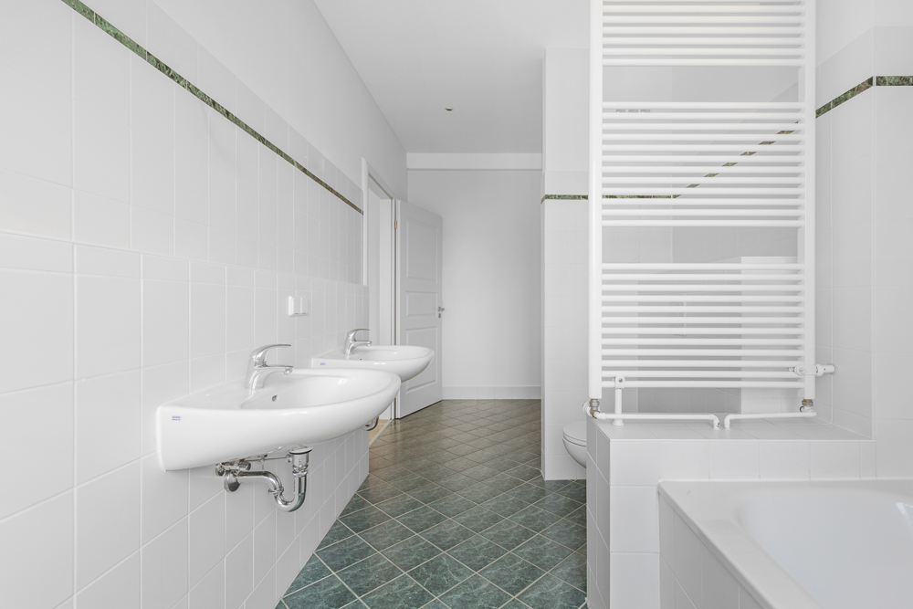 Helles Badezimmer mit zwei Waschbecken, Badewanne und Handtuchheizkörper.
