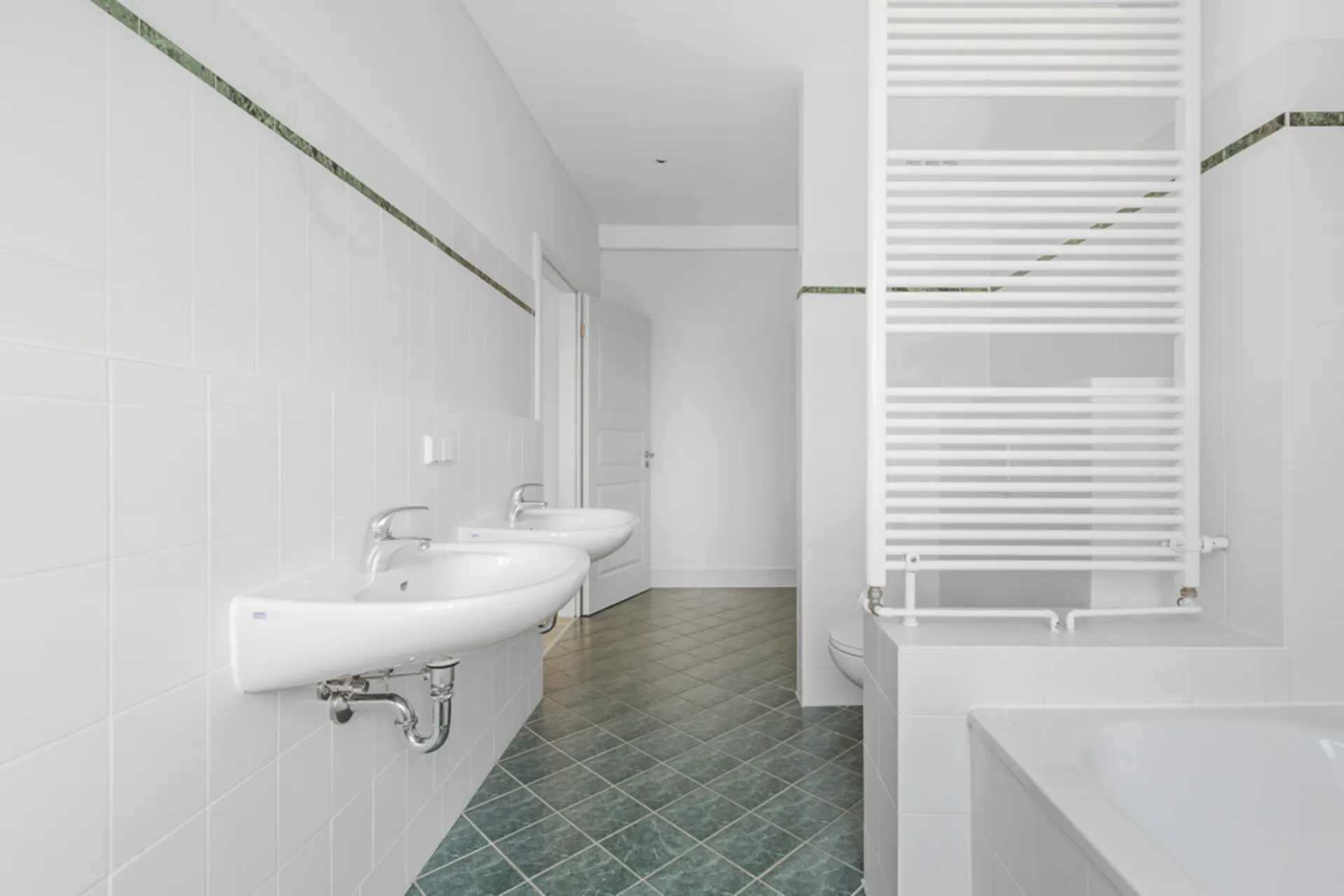 Helles Badezimmer mit zwei Waschbecken, Badewanne und Handtuchheizkörper.