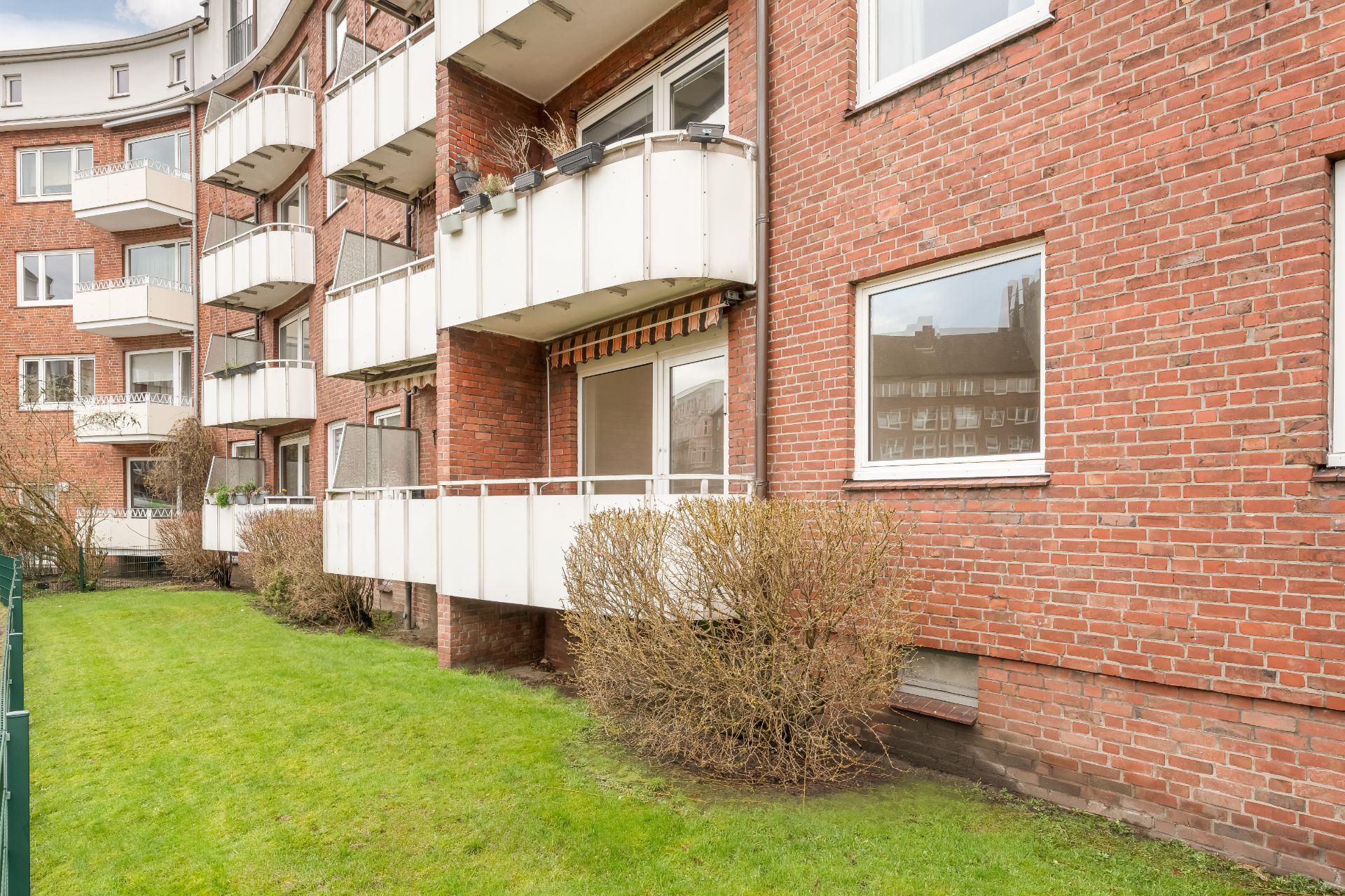 Mehrstöckiges Wohngebäude mit Backsteinfassade, Balkonen und grünem Rasen im Vordergrund.