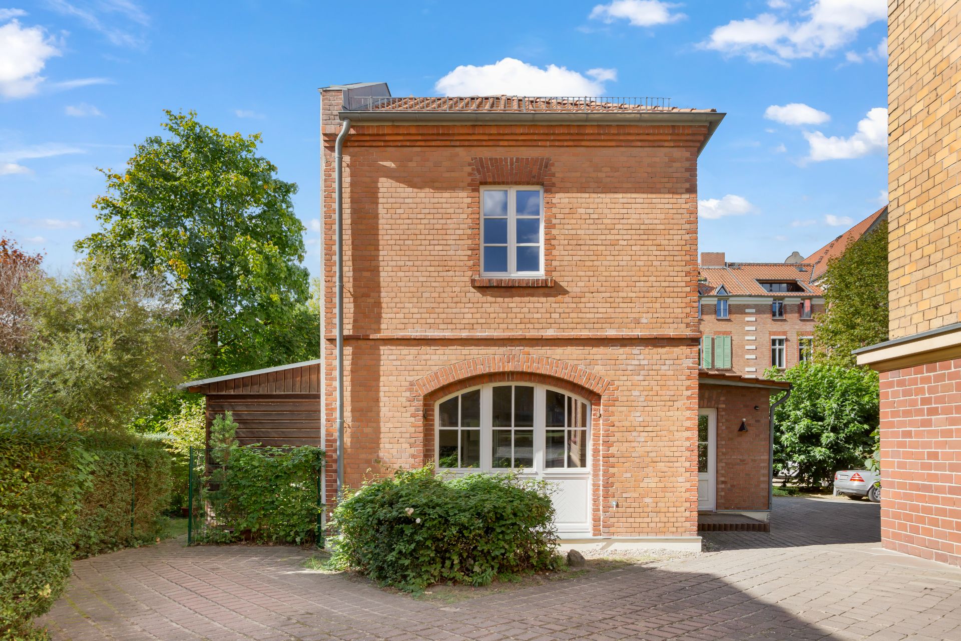 Backsteinwohnhaus mit Fenster und Tür, umgeben von Grün und gepflastertem Weg.