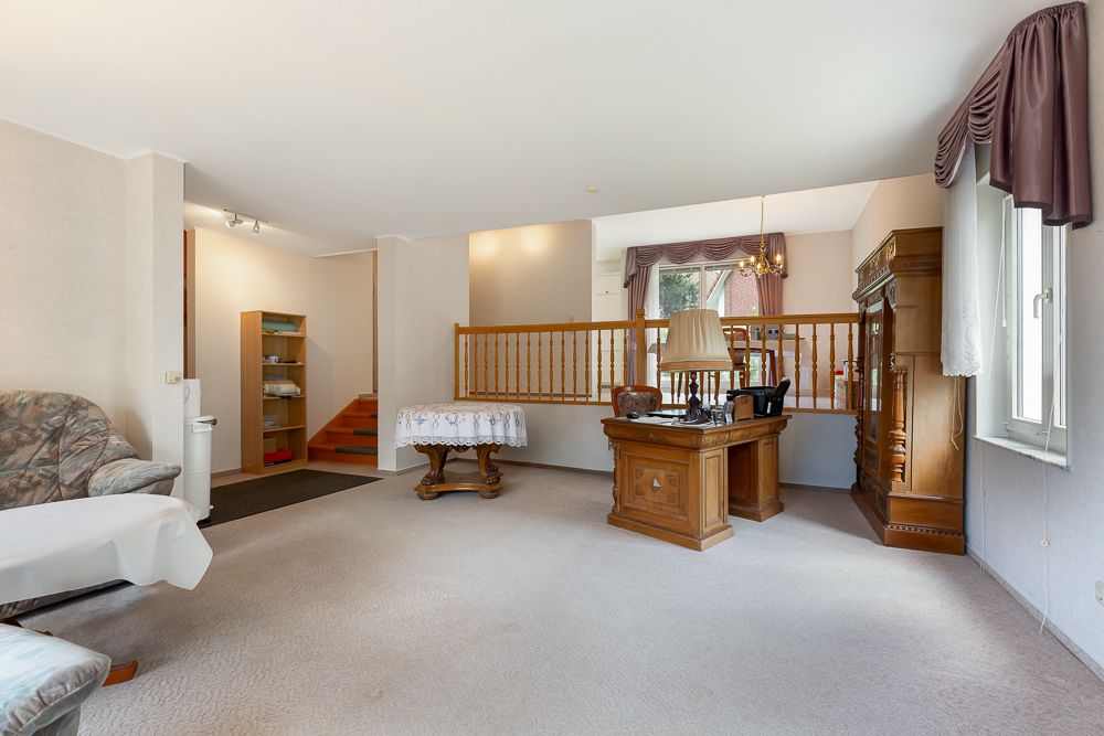 Helles Wohnzimmer mit Sitzbereich, Holzmöbeln und einer kleinen Treppe zur erhöhten Ebene.