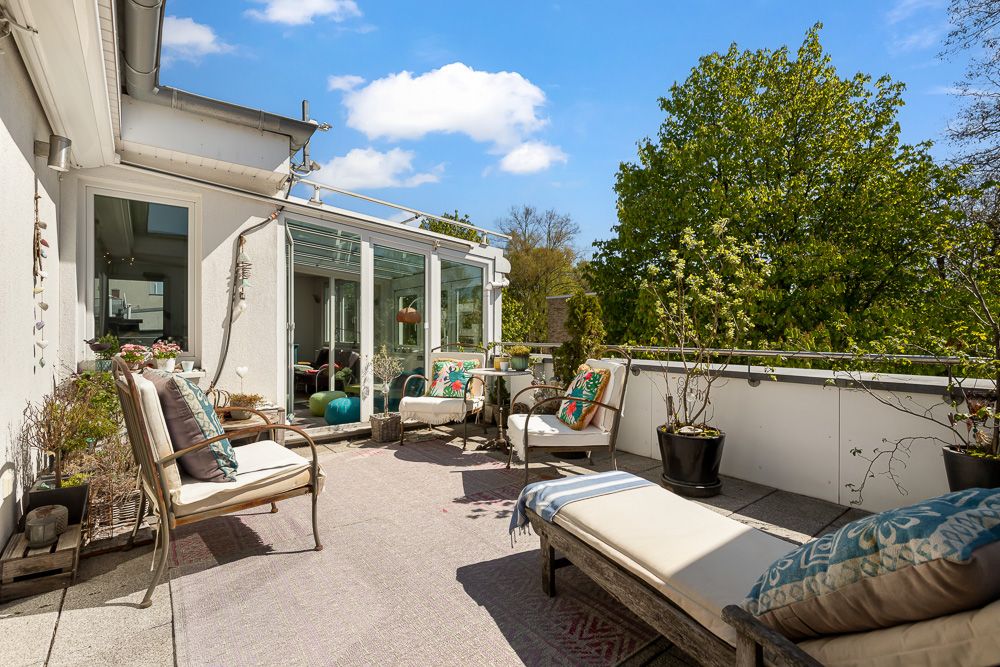 Gemütliche Terrasse mit Sitzgelegenheiten, Pflanzen und Blick auf grüne Bäume.