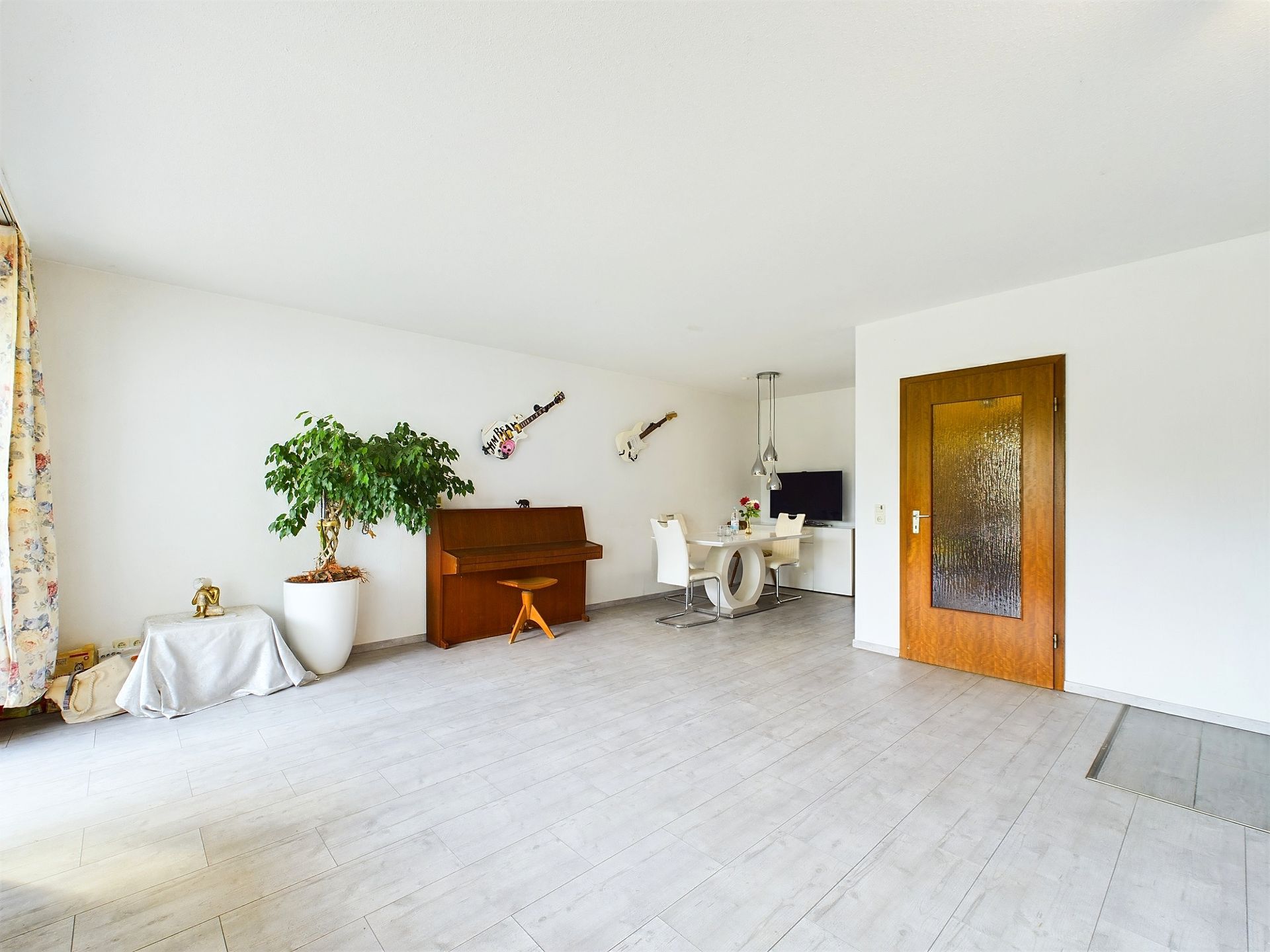 Helles Wohnzimmer mit Klavier, Esstisch, Fernseher und Topfpflanze.