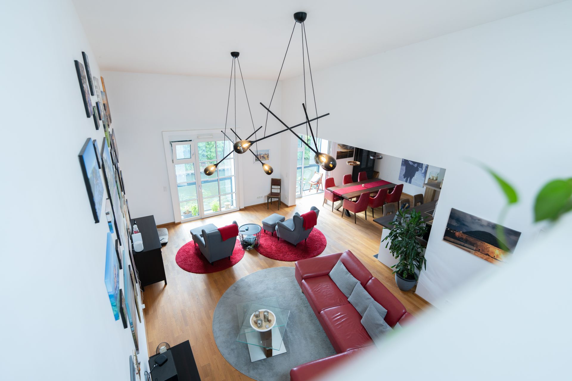 Modernes Wohnzimmer mit roten Möbeln, großem Fenster, Esstisch und Wandbildern, von oben gesehen.