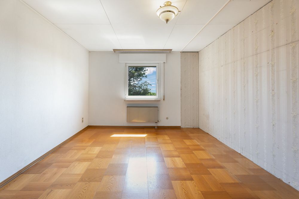 Leerer Raum mit Holzboden, einem Fenster und weißer Deckenlampe.