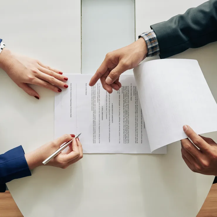 Zwei Personen besprechen und unterschreiben ein Dokument an einem weißen Tisch.