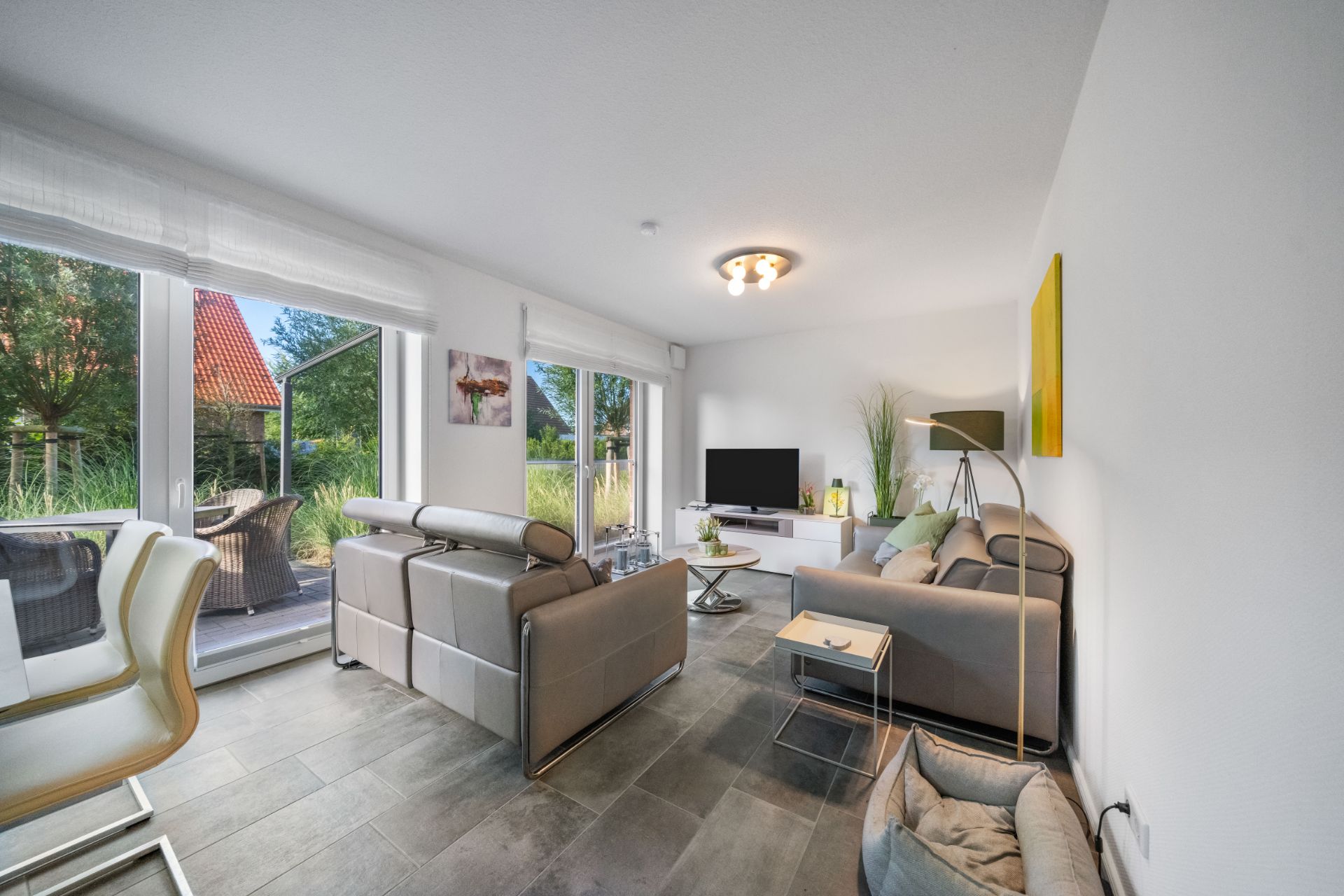 Modernes Wohnzimmer mit großen Fenstern, grauen Sofas und Fernseher, Zugang zur Terrasse.