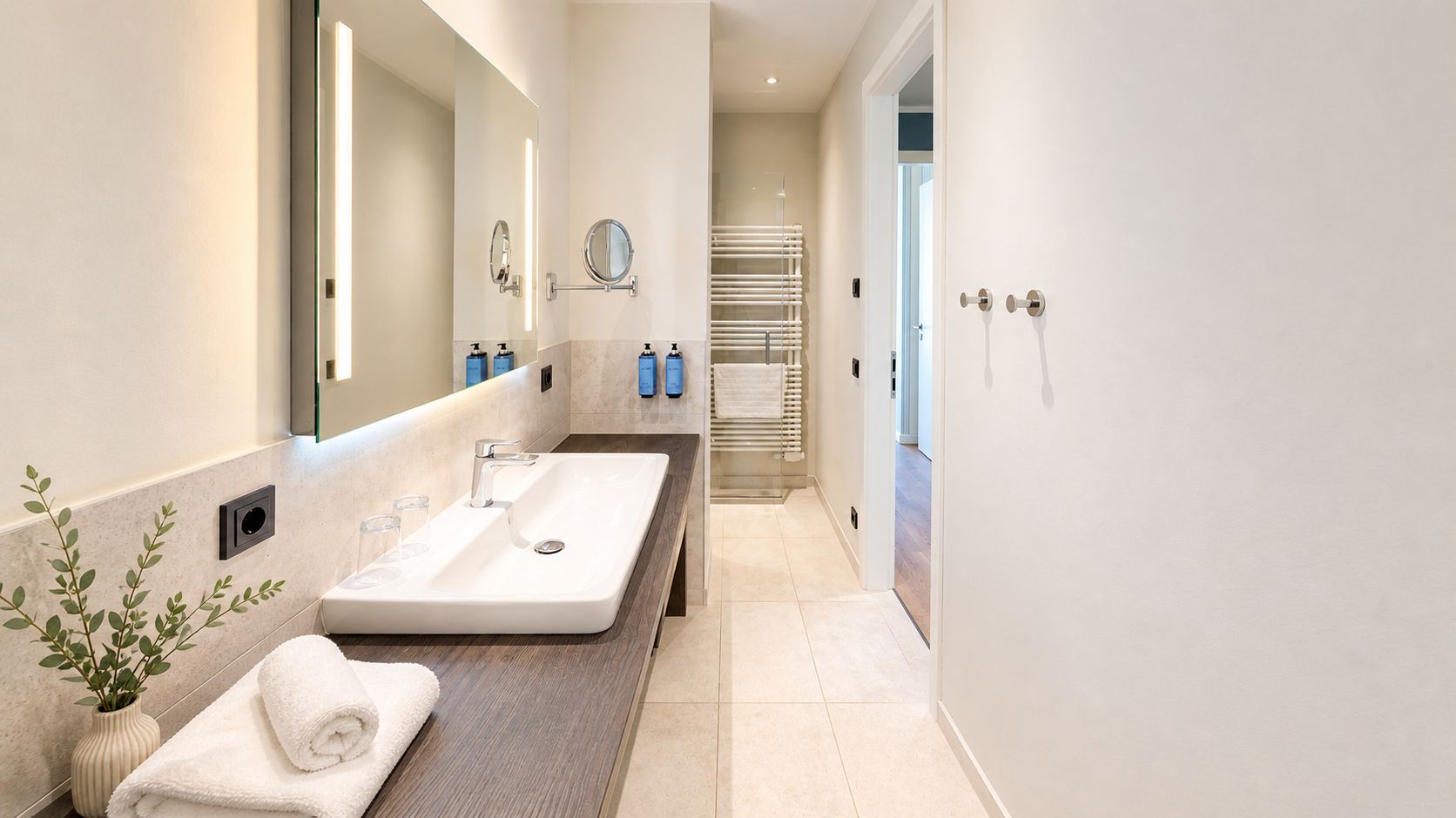 Modernes Badezimmer mit langem Waschtisch, Spiegel, Handtuchhalter und gefliestem Boden.