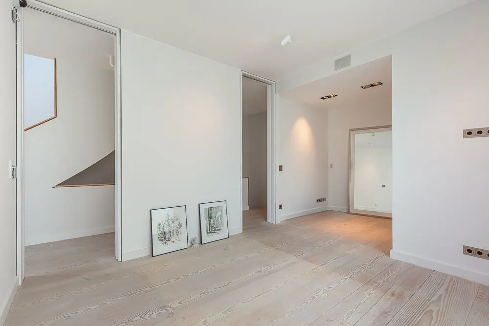 Helles, leeres Zimmer mit Holzboden, zwei Bildern an der Wand und Blick auf eine Treppe.