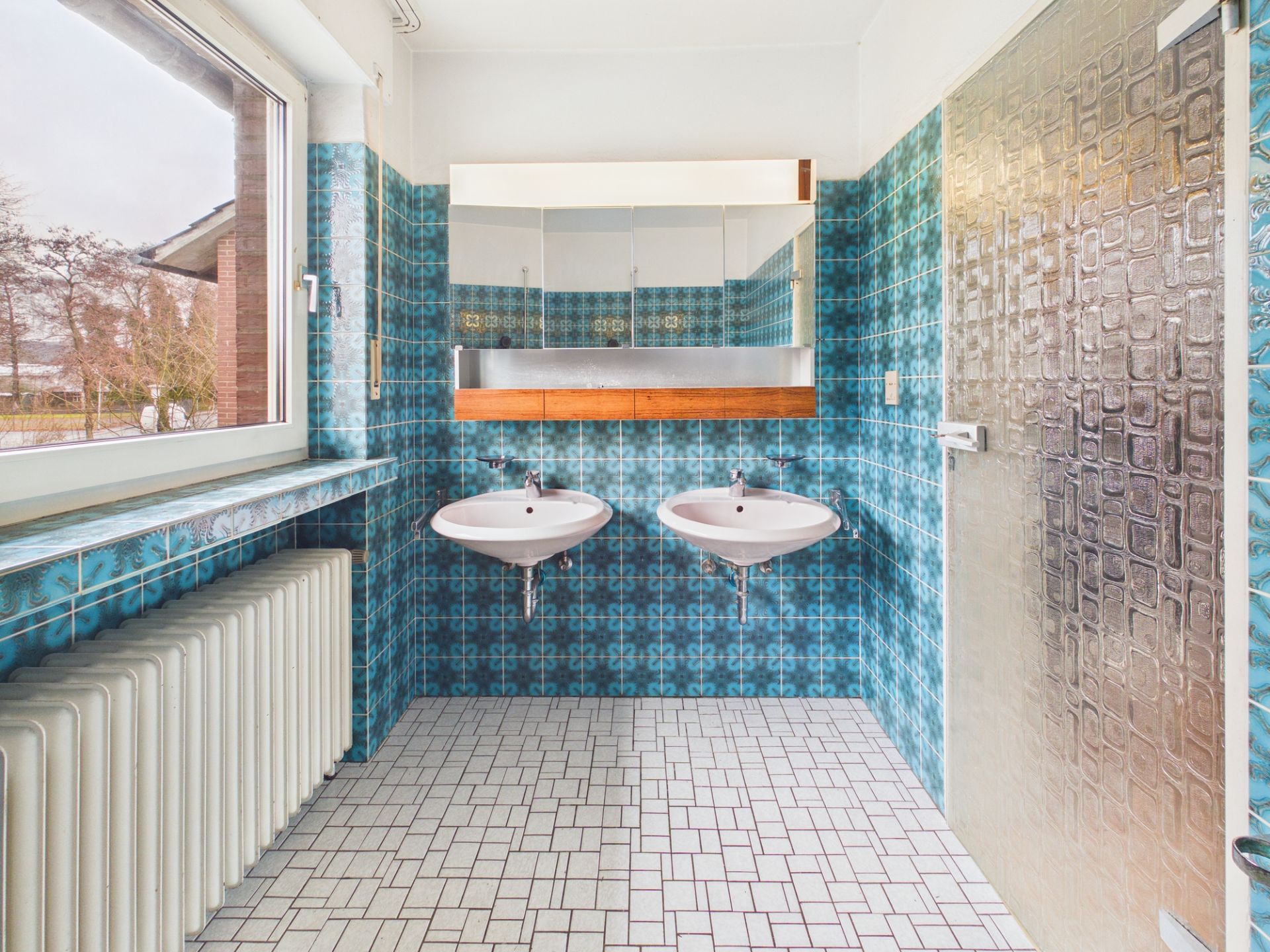 Badezimmer mit zwei Waschbecken, blau gemusterten Fliesen und großem Fenster.