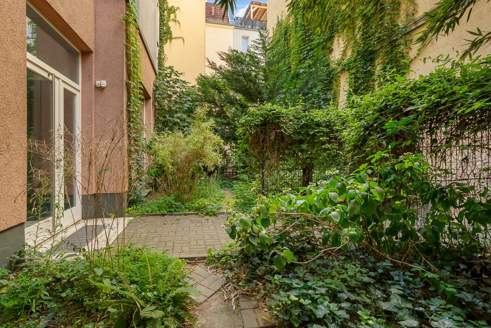 Begrünter Innenhof mit Pflasterweg und dichter Bepflanzung an einem Wohngebäude.