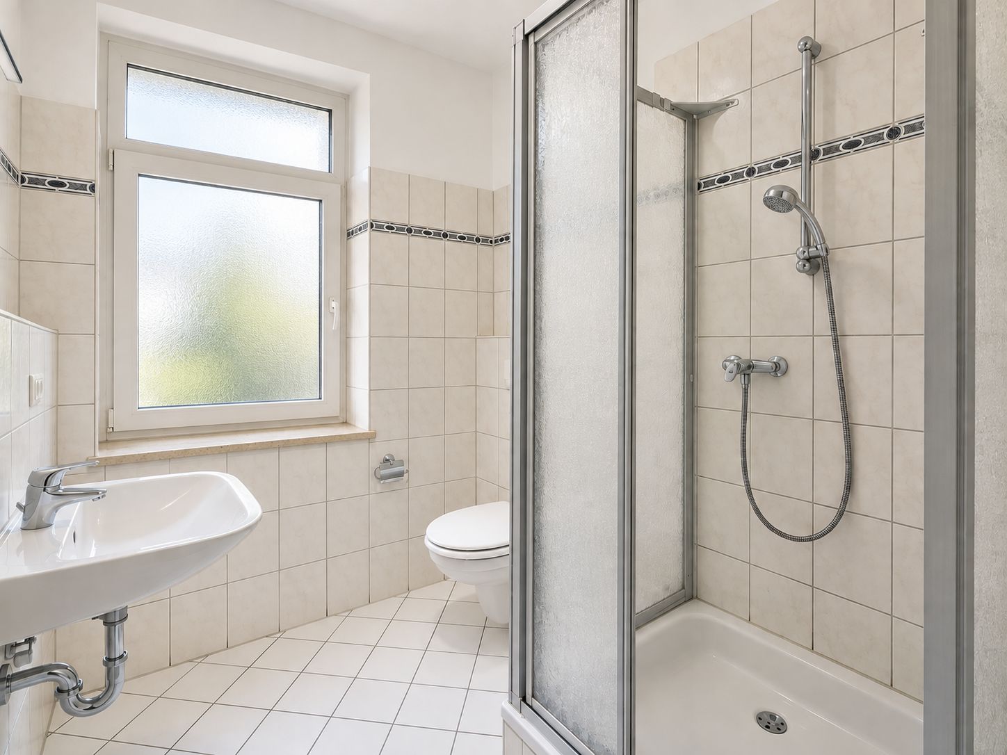 Helles Badezimmer mit Fenster, Dusche, Waschbecken und Toilette.