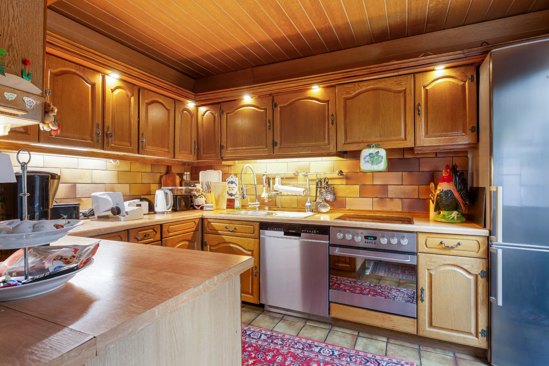Holzküche mit Einbaugeräten, Spüle, Herd, Kühlschrank und rotem Teppich auf dem Boden.