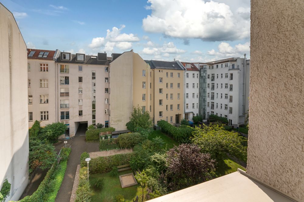 Blick von einem Balkon auf einen begrünten Innenhof mit mehreren Wohngebäuden.