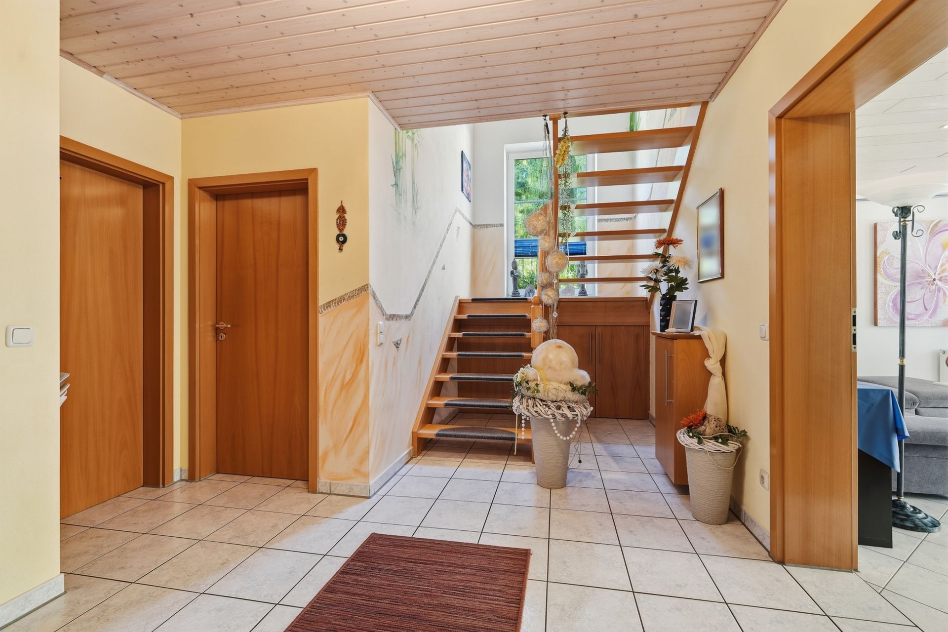 Heller Flur mit Treppe, Fliesenboden, Holztüren und Dekorationen.