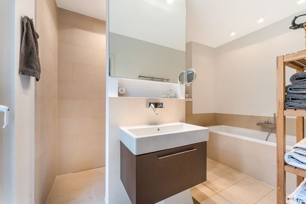 Modernes Badezimmer mit Waschbecken, Spiegel, Badewanne, Dusche und Regal mit Handtüchern.