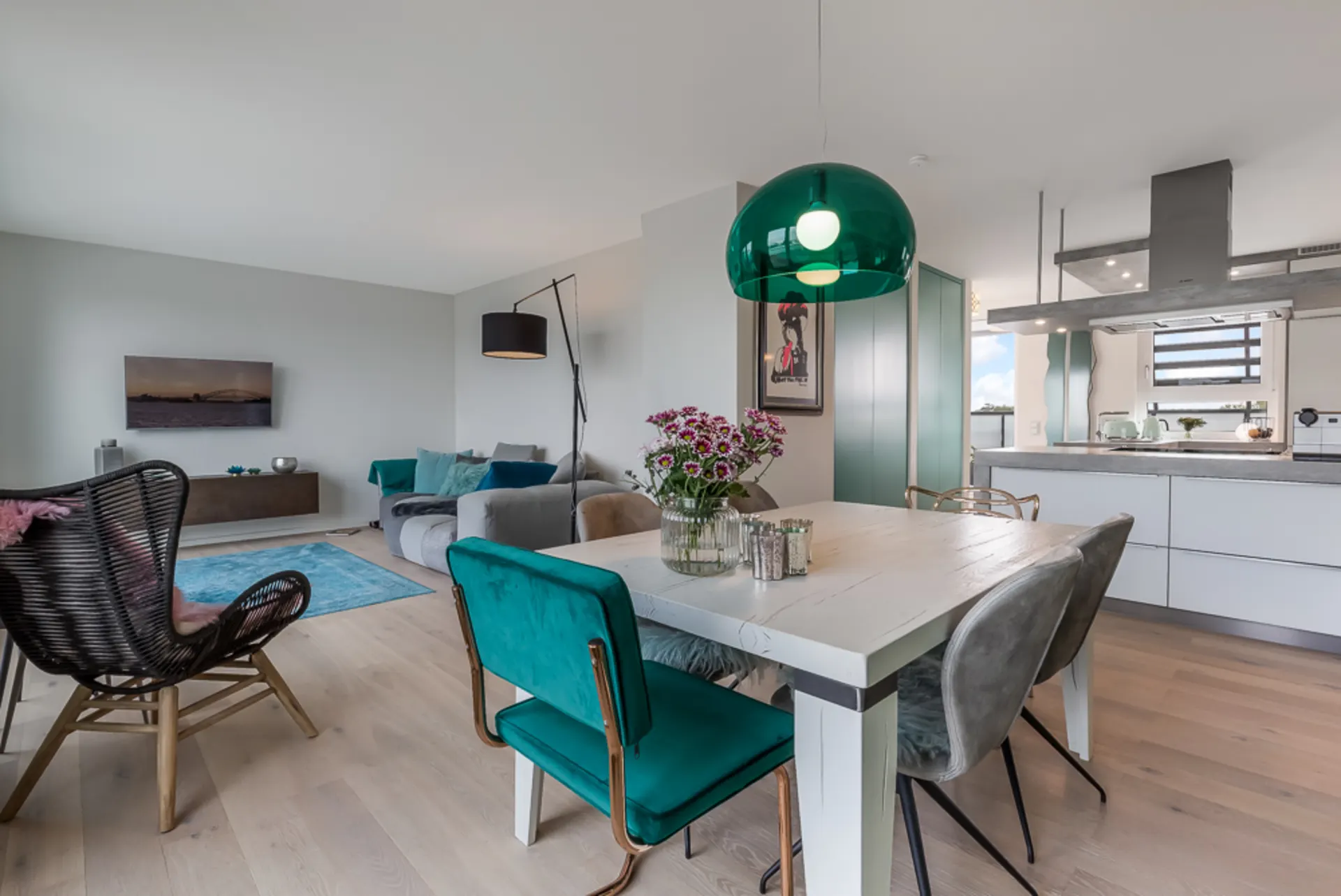 Modernes Wohnzimmer mit Essbereich, Küche im Hintergrund, grüne Lampe, Blumen auf dem Tisch.
