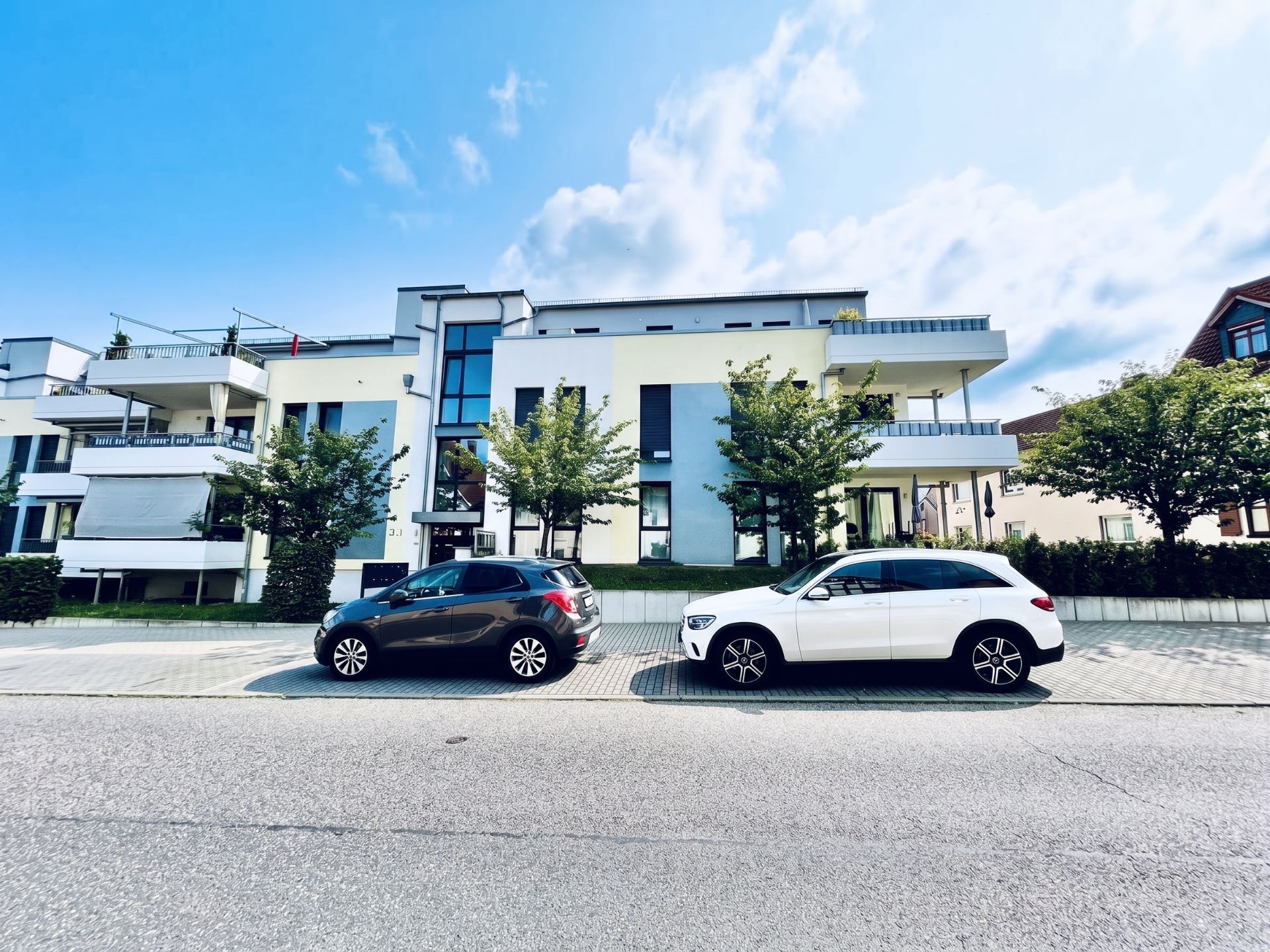 Modernes Mehrfamilienhaus mit Balkonen und zwei geparkten Autos vor dem Gebäude.