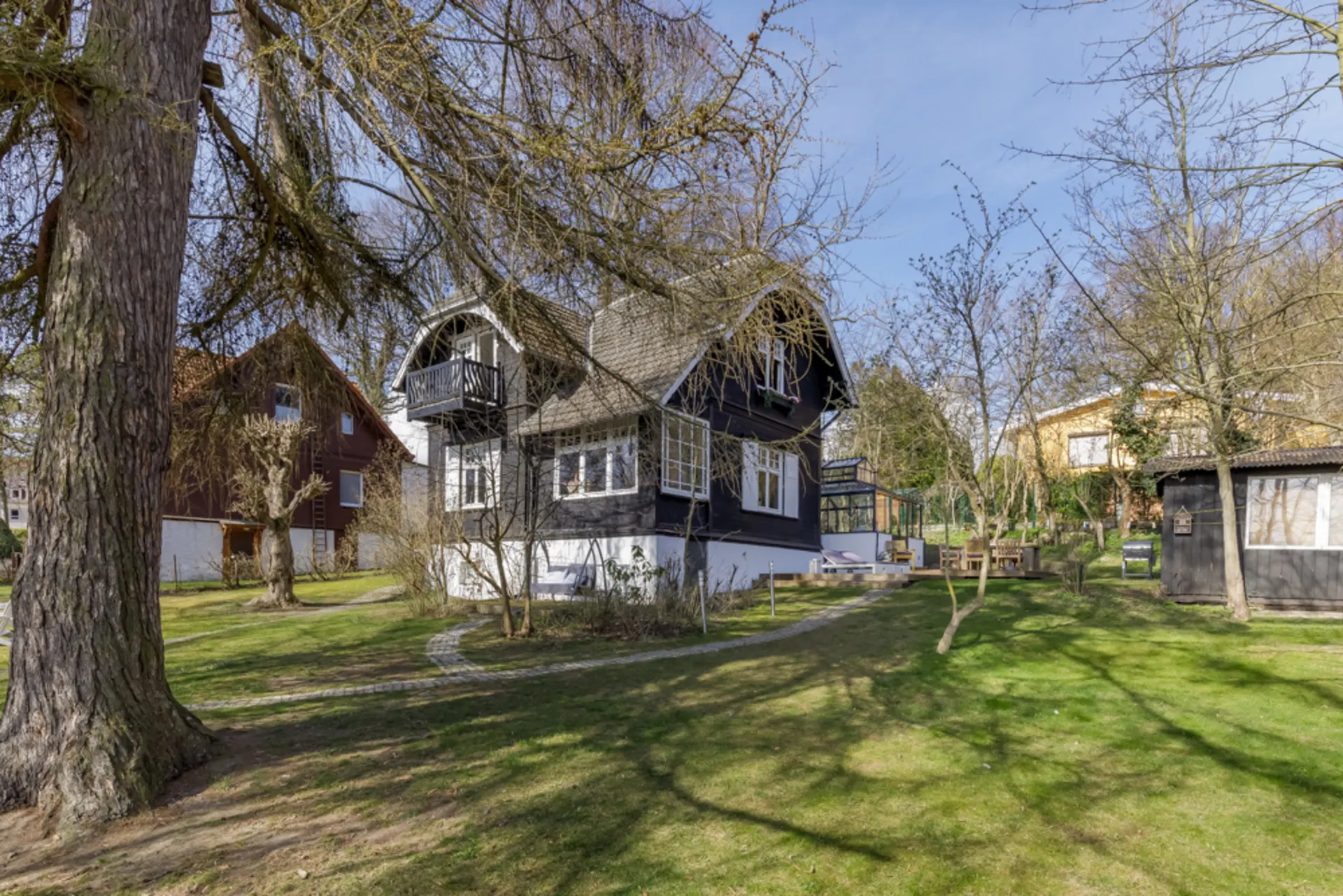 Zweistöckiges Haus mit dunkler Fassade, großem Garten und Bäumen im Vordergrund.