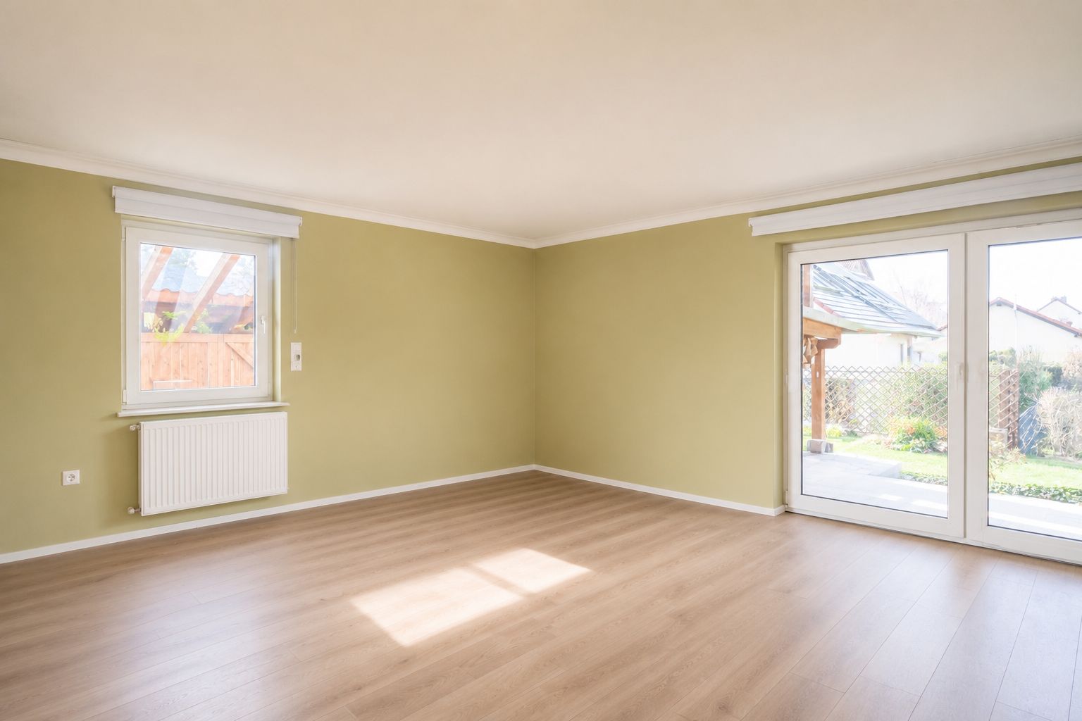 Leerer, heller Raum mit Holzboden, Fenster und Glastür zum Garten.