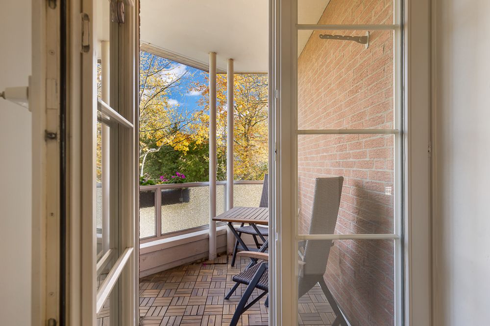 Balkon mit zwei Stühlen und einem kleinen Tisch, Blick auf Bäume mit Herbstlaub.
