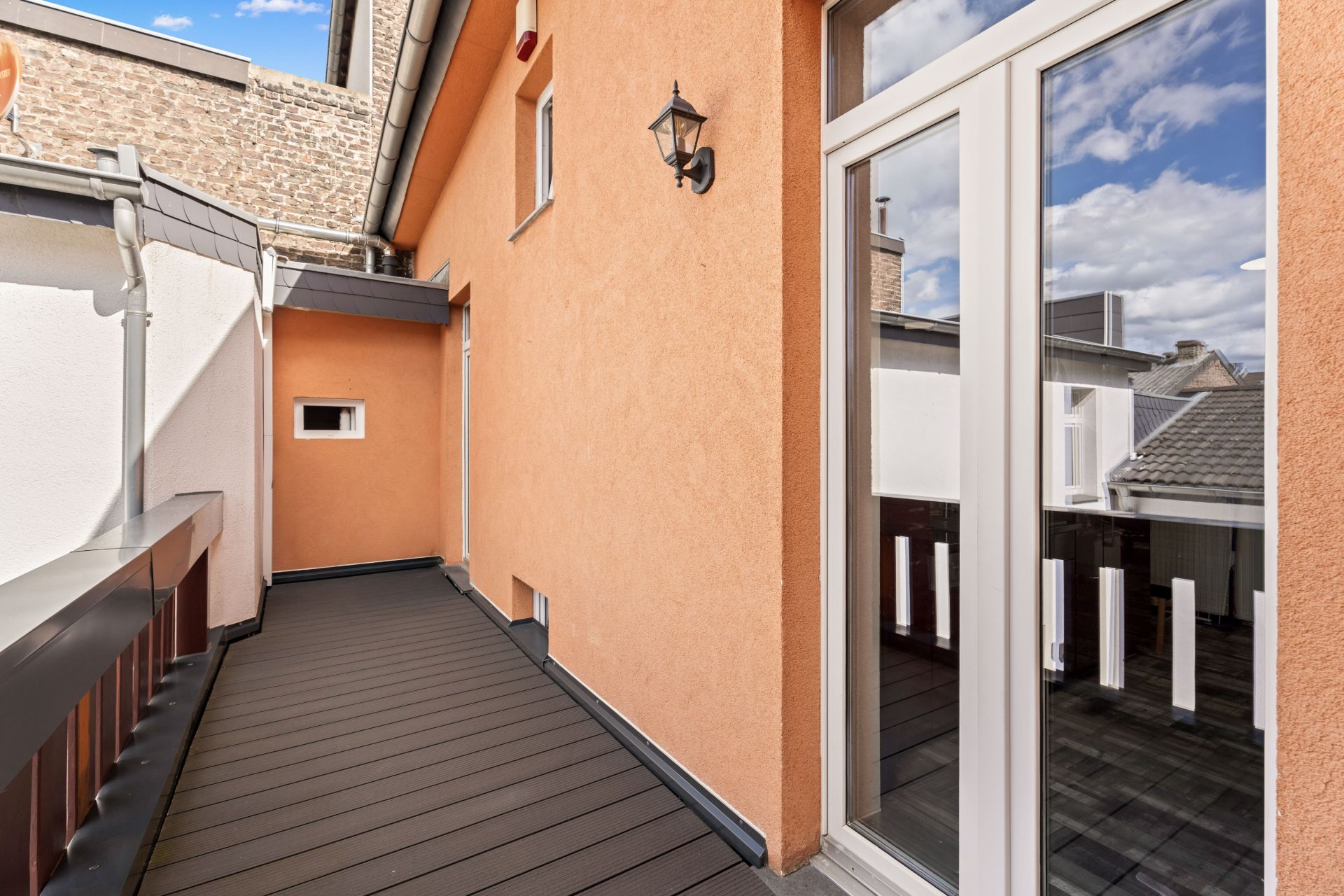 Schmaler Balkon mit braunem Geländer, orangefarbener Wand und weißer Tür, Blick auf Nachbargebäude.