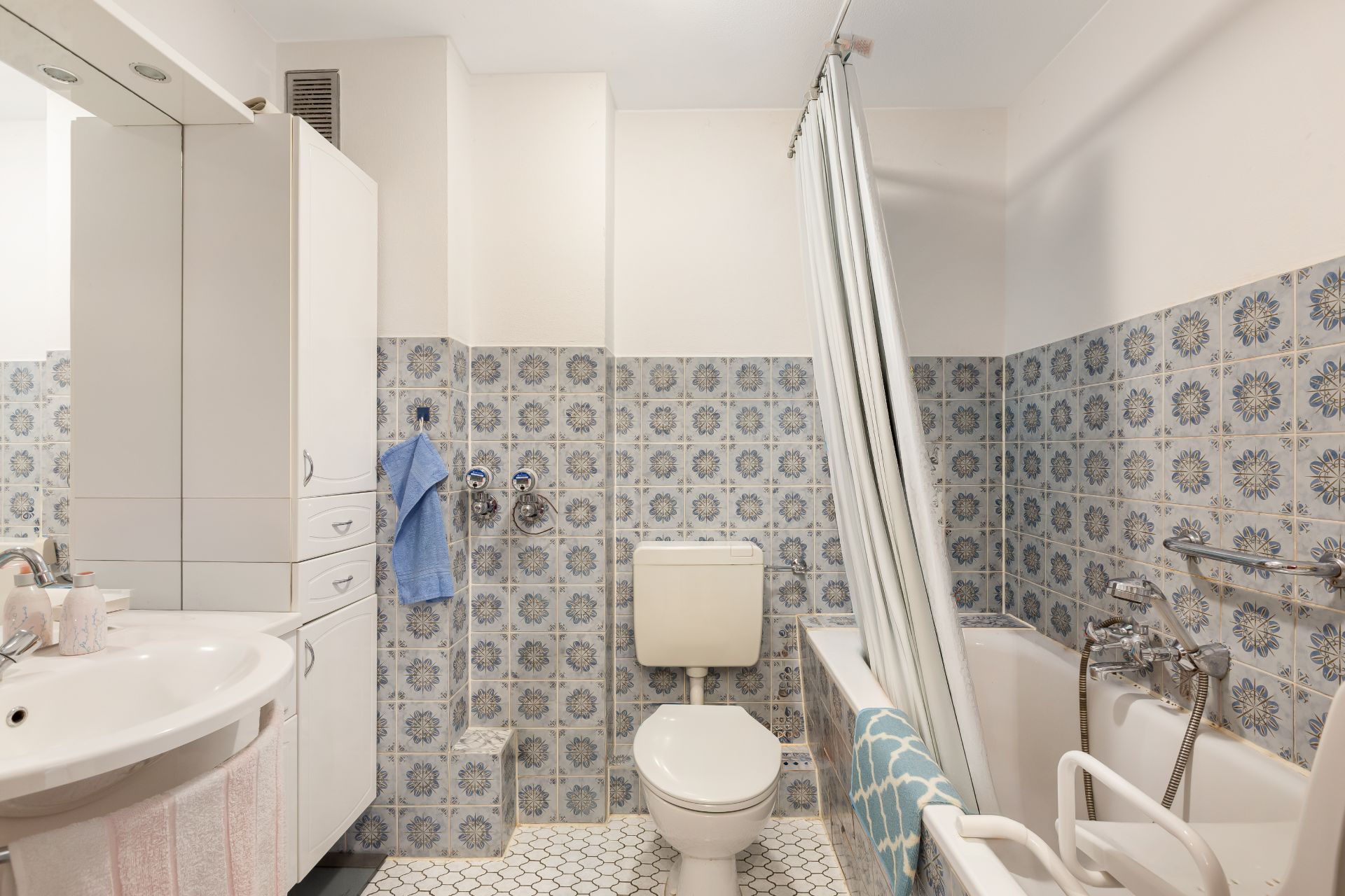Helles Badezimmer mit gemusterten Fliesen, Waschbecken, Toilette und Badewanne mit Duschvorhang.