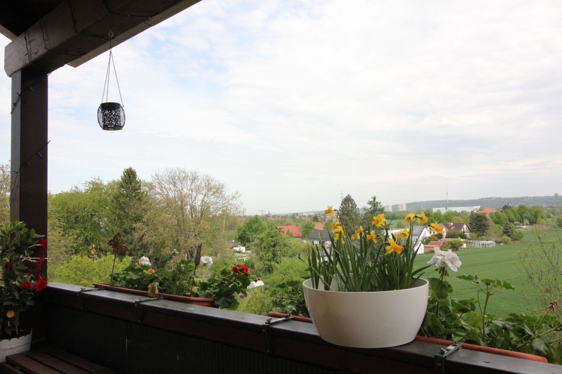 Balkon mit Blumenkästen und Blick auf grüne Landschaft und Häuser im Hintergrund.