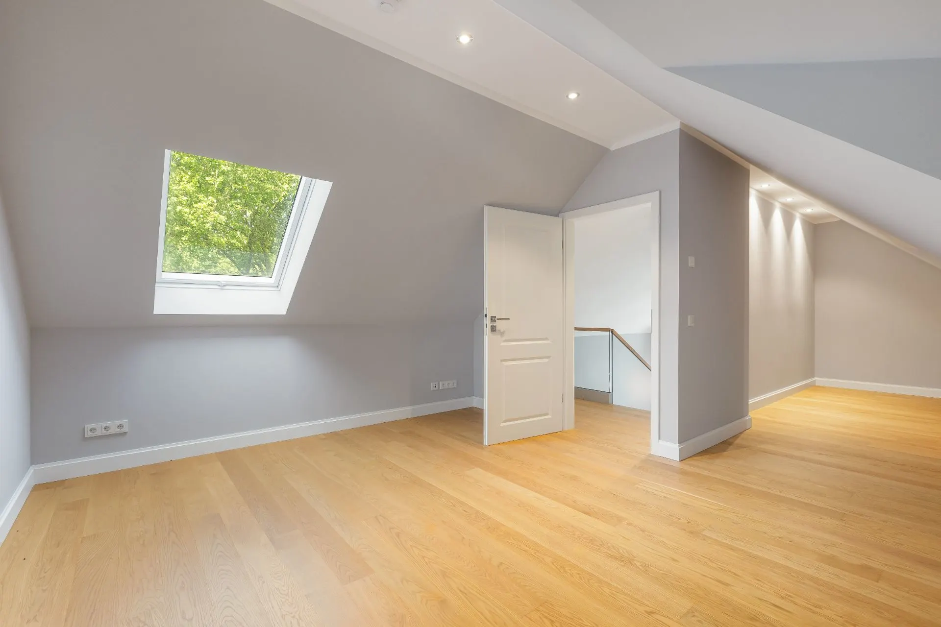 Helles Zimmer mit Dachschräge, Holzfußboden, offenem Fenster und weißer Tür.