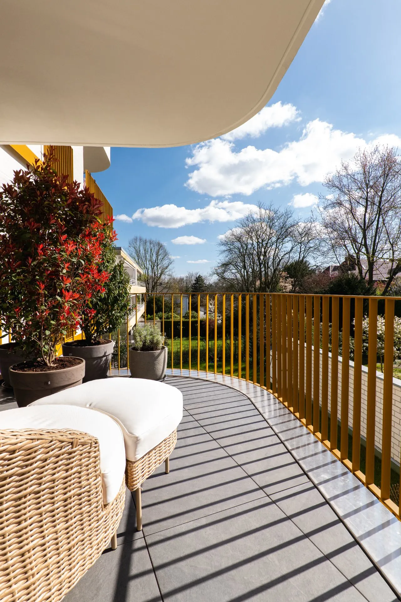 Moderner Balkon mit gelbem Geländer, Pflanzen in Töpfen und Sitzmöbeln, Blick ins Grüne.