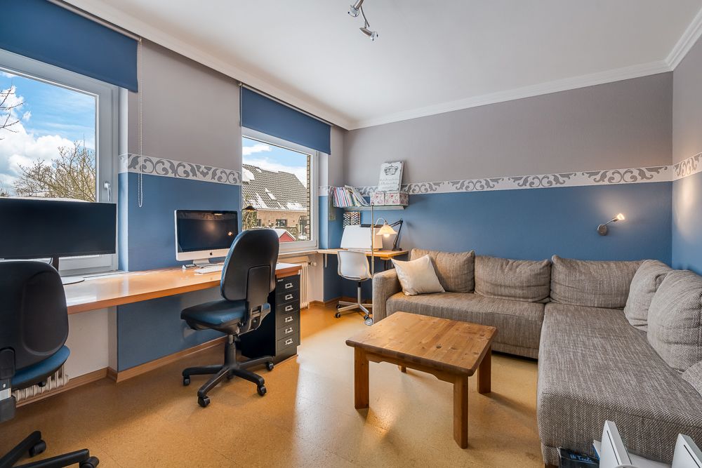 Modernes Arbeitszimmer mit Schreibtischen, Computer, grauem Ecksofa und Couchtisch.