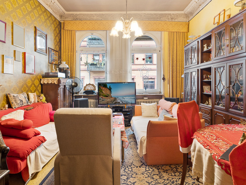 Wohnzimmer mit mehreren Sofas, Sessel, großem Schrank, Fernseher und Kronleuchter.