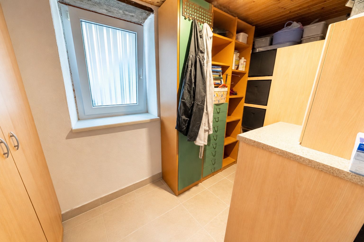 Hauswirtschaftsraum mit Fenster, Holzregalen, Schränken und Fliesenboden.
